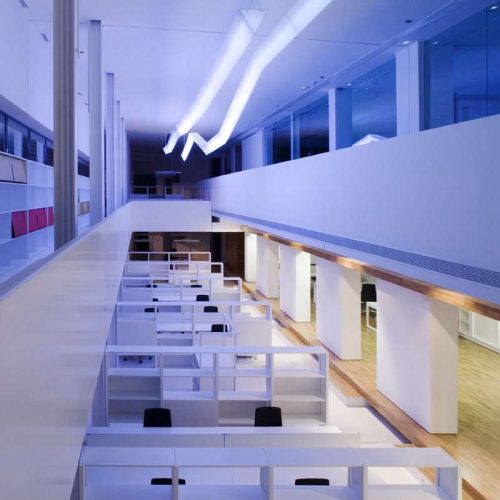 Oficina moderna y minimalista con espacios de trabajo en cubículos, iluminación contemporánea y paredes blancas, diseñada para fomentar la productividad y la colaboración.